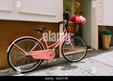 Vintage bicicletta rosa decorativa con un cesto di fiori sul parcheggio flowersIn città europea Foto Stock