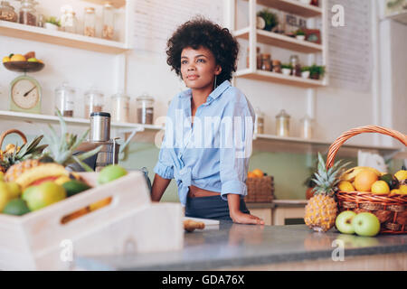 Ritratto di attraente giovane donna in piedi al bar dei succhi contatore. Africana dei dipendenti di sesso femminile a juice bar che guarda lontano. Foto Stock