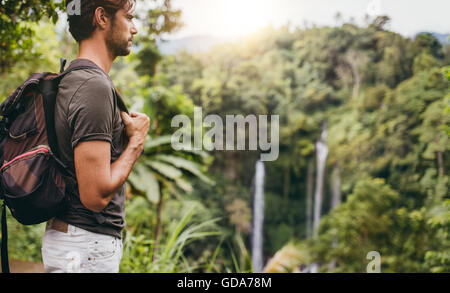 Vista laterale colpo di giovane uomo con zaino escursioni nella natura. Escursionista maschio vicino a cascata nella foresta. Foto Stock