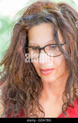 Splendida donna di mezza età in un abito rosso e marrone lungo i capelli ondulati è la lettura che indossa un paio di occhiali da stupidi Foto Stock