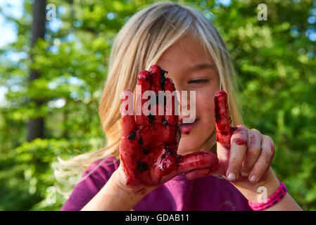 Carina ragazza bionda che mostra le mani cosparse con mirtilli di bosco. Estate e per il divertimento di tutta la famiglia. Foto Stock