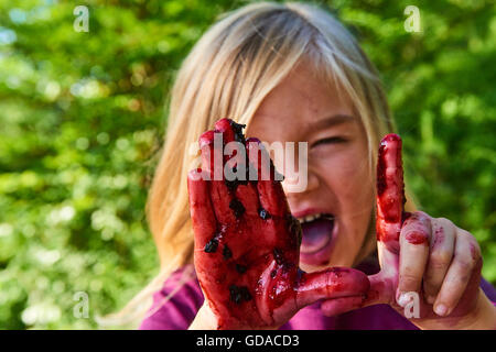 Carina ragazza bionda che mostra le mani cosparse con mirtilli di bosco. Estate e per il divertimento di tutta la famiglia. Foto Stock