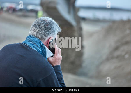 Grigio uomo dai capelli sul telefono cellulare con sfondo sfocato Foto Stock