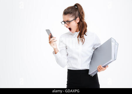 Angry mad giovane imprenditrice in vetri tramite telefono cellulare e gridando su sfondo bianco Foto Stock