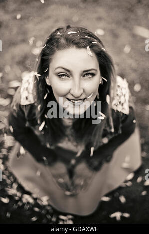 Petali di fiori che cade su di giovane donna seduta sull'erba Foto Stock