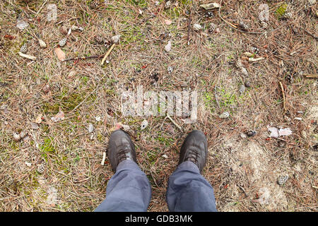 Voce maschile in piedi in scarpe marrone permanente sulla sporca terra foresta, prospettiva in prima persona Foto Stock