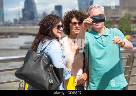 L'uomo prendendo un selfie con due donne con vedute di Londra in luglio Foto Stock