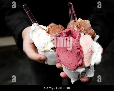 Una persona che tiene in mano due tazze riempite con vari gusti di gelato, tra cui cioccolato, vaniglia e bacche, tenendo in mano una tazza di gelato Foto Stock