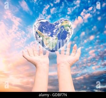 Mondo in forma di cuore con sopra le donne le mani umane su sfocato sfondo naturale: Mondo Salute del cuore giorno,Elemento di questa immagine fur Foto Stock
