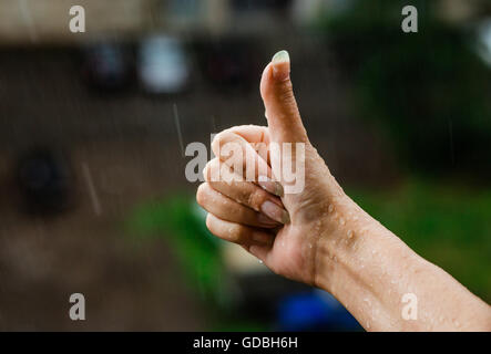Pollice in alto segno con le mani bagnate a pioggia. Ambientale e tempo piovoso concept Foto Stock