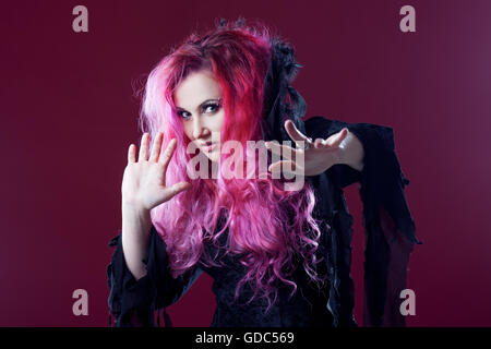 Scary strega con i capelli rossi esegue magic su uno sfondo di colore rosa. Halloween, tema horror. Foto Stock