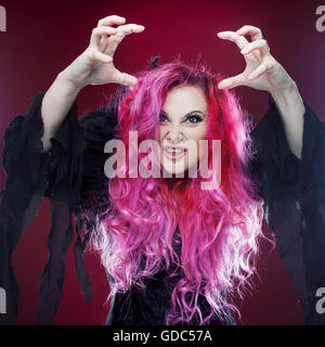 Scary strega con i capelli rossi esegue magic su uno sfondo di colore rosa. Halloween, tema horror. Foto Stock