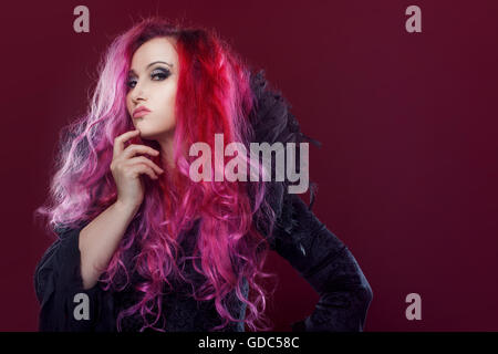 Scary strega con i capelli rossi esegue magic su uno sfondo di colore rosa. Halloween, tema horror. Foto Stock