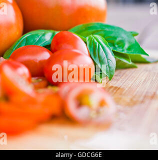 Tritate i pomodori ciliegini e basilico su un tagliere Foto Stock