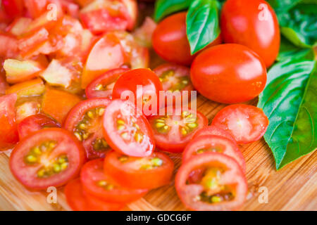 Tritate i pomodori ciliegini e basilico su un tagliere Foto Stock