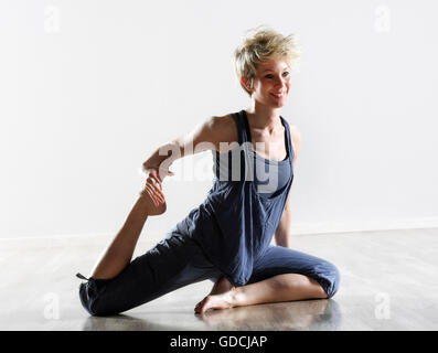 Felice a piedi nudi giovane donna bionda facendo esercizi di stretching sul pavimento come lei gode del suo allenamento quotidiano Foto Stock