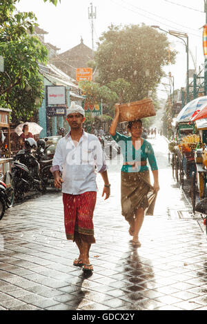 Indonesian l uomo e la donna in abiti tradizionali a piedi sotto la pioggia sulla strada di Kuta, Indonesia Foto Stock