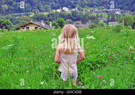 Ragazzo biondo nel campo di erba in cerca di casa Foto Stock