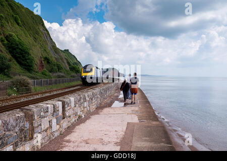 La gente camminare lungo la parete del mare con un avvicinamento 125 treno a Teignmouth vicino a Dawlish, Devon, Inghilterra. Foto Stock