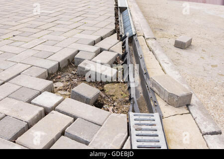 La distruzione del passaggio pedonale di pavimentazione con il drenaggio e la strada concreta Foto Stock