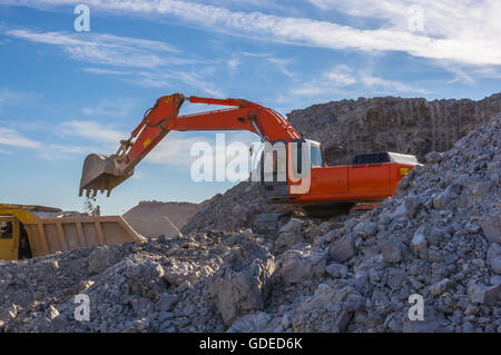 Escavatore e dumper - magazzino produzione nella cava di argilla blu su sfondo cielo Foto Stock