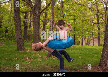 Due giovani ragazzi giocare su tire swing in foresta Foto Stock