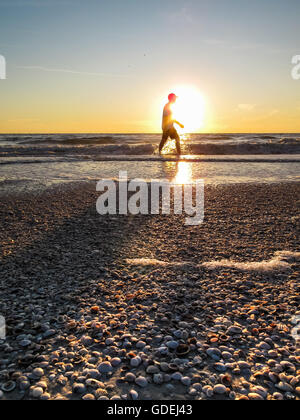 Uomo che cammina lungo la spiaggia al tramonto, Florida, Stati Uniti Foto Stock