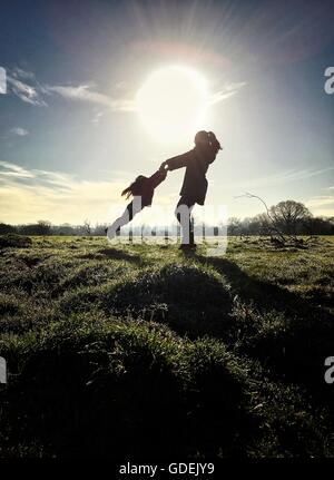 Silhouette di madre figlia oscillante nel campo Foto Stock