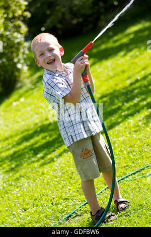 Little Boy giocando con un tubo flessibile di acqua in giardino Foto Stock