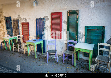 Vecchi tavoli e posti a sedere sulla strada. Verde e tavoli bianchi e bianco e viola sedi nei pressi di blu, verde e rosso di windows su una strada io Foto Stock