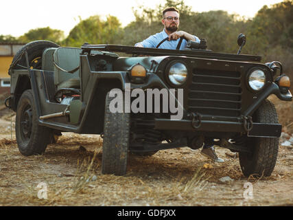 Giovane uomo elegante con gli occhiali e il filtro bow tie vicino alla vecchia SUV sul tramonto Foto Stock