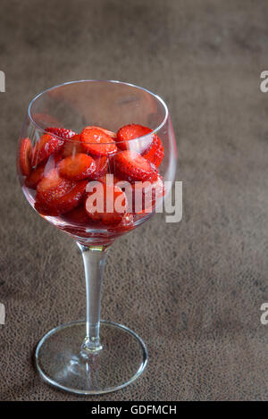 Fragole a fette in un bicchiere di vino su uno sfondo marrone Foto Stock