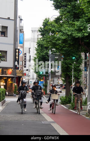 Ragazzi in uniformi di baseball di cavalcare le loro biciclette sul marciapiede nel centro cittadino di Osaka. Foto Stock