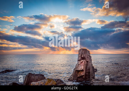 Tramonto su una spiaggia rocciosa. Le nuvole colorate riflettendo in mare. Foto Stock