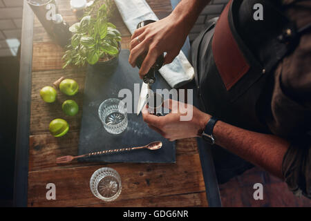 Close up di barman mani versando la bevanda alcolica in un jigger per preparare un cocktail, con le foglie di basilico e limoni sulla barra c Foto Stock