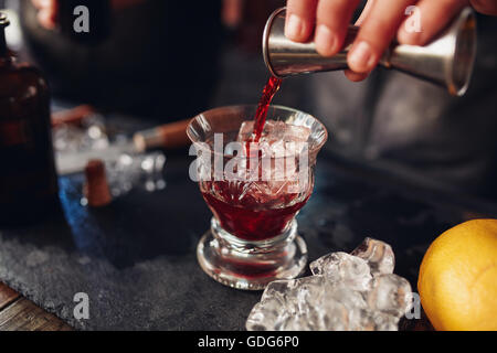 Immagine ravvicinata di barman versa manualmente da bere una tazza di misura in un cocktail di vetro riempita con cubetti di ghiaccio. Il barman prepara f Foto Stock