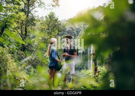 Colpo all'aperto del giovane uomo e donna in piedi insieme su una scogliera e parlare. Paio di escursionisti insieme in una foresta con acqua f Foto Stock