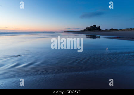 Il castello di Bambburgh si riflette in parte nella sabbia bagnata della spiaggia come il ritiro delle onde, la spiaggia di Bambburgh Foto Stock