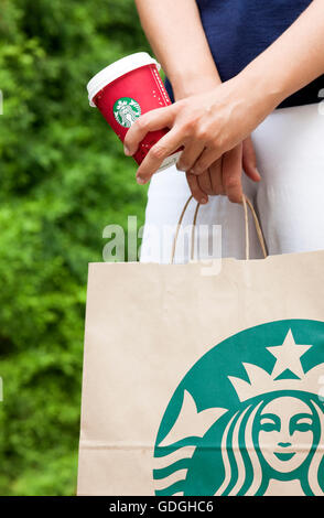 Paphos, Cipro - 23 novembre 2013 Donna in strada con Starbucks takeaway sacchetto di carta e carta rossa tazza di caffè nelle sue mani. Foto Stock