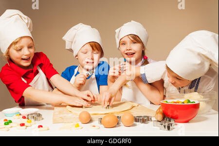 Quattro piccoli fornai utilizzando cookie cutters Foto Stock