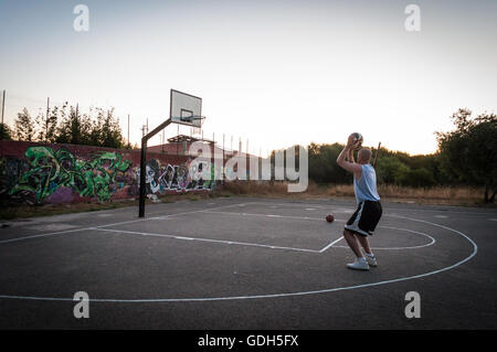 Giocatore di basket in città parco giochi al tramonto Foto Stock