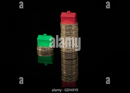 Casa / alloggiamento / prezzo proprietà concetto di inflazione. Giocattolo di colorate case poste su pile di vecchio stile di libbra di monete su sfondo nero. Foto Stock