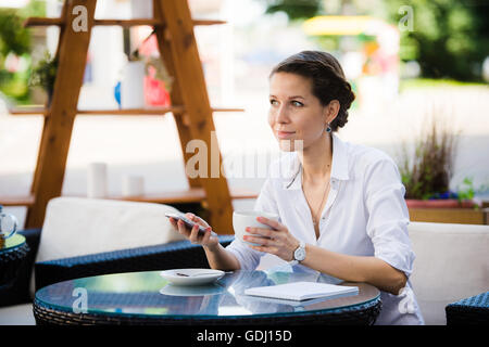 Ritratto di una imprenditrice utilizzando smart phone nel cafè sul marciapiede. Foto Stock