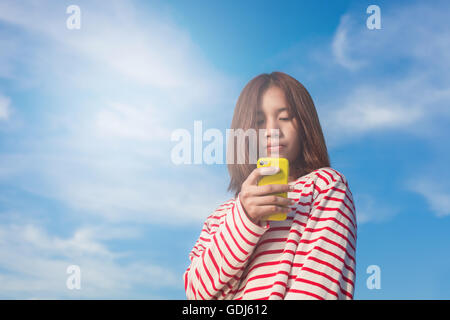 Ritratto di giovane donna utilizza lo smartphone sul cielo blu sullo sfondo. Foto Stock