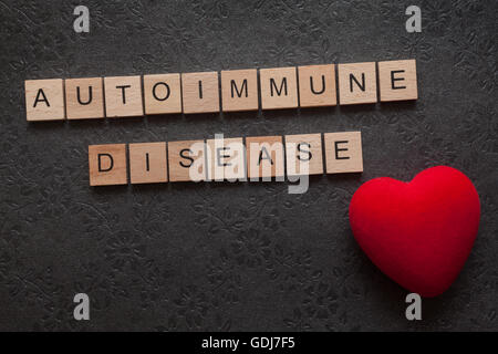 La parola malattia autoimmune formato con lettere in legno e un cuore su sfondo scuro Foto Stock