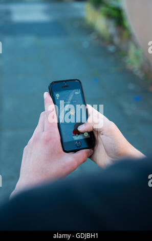 Adolescente utilizzando un telefono cellulare per giocare gioco basato sulla realtà aumentata Pokemon vai Foto Stock