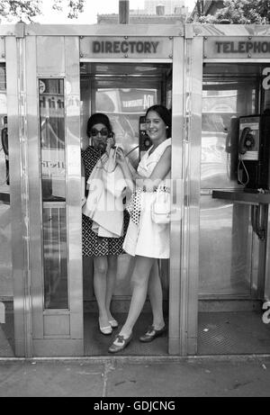 Due donne godetevi la privacy di una cabina telefonica nel centro di Manhattan nel 1969. Foto Stock