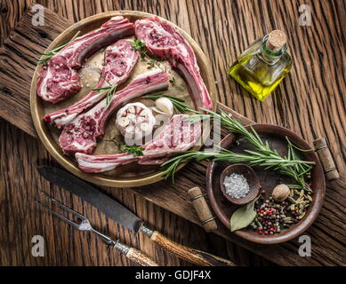 Materie costolette di agnello con aglio ed erbe aromatiche sul vecchio tavolo in legno. Foto Stock