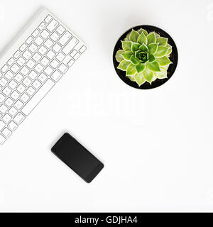 Ufficio bianco scrivania con connessione wireless a tastiera in alluminio, smart phone con schermo nero e succulenta fiore in pentola. Vista superiore wit Foto Stock