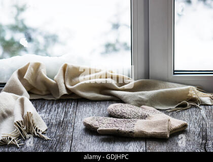 Beige sciarpa di lana e muffole situato sul legno stilizzata davanzale. Inverno concetto di comfort e relax. Foto Stock